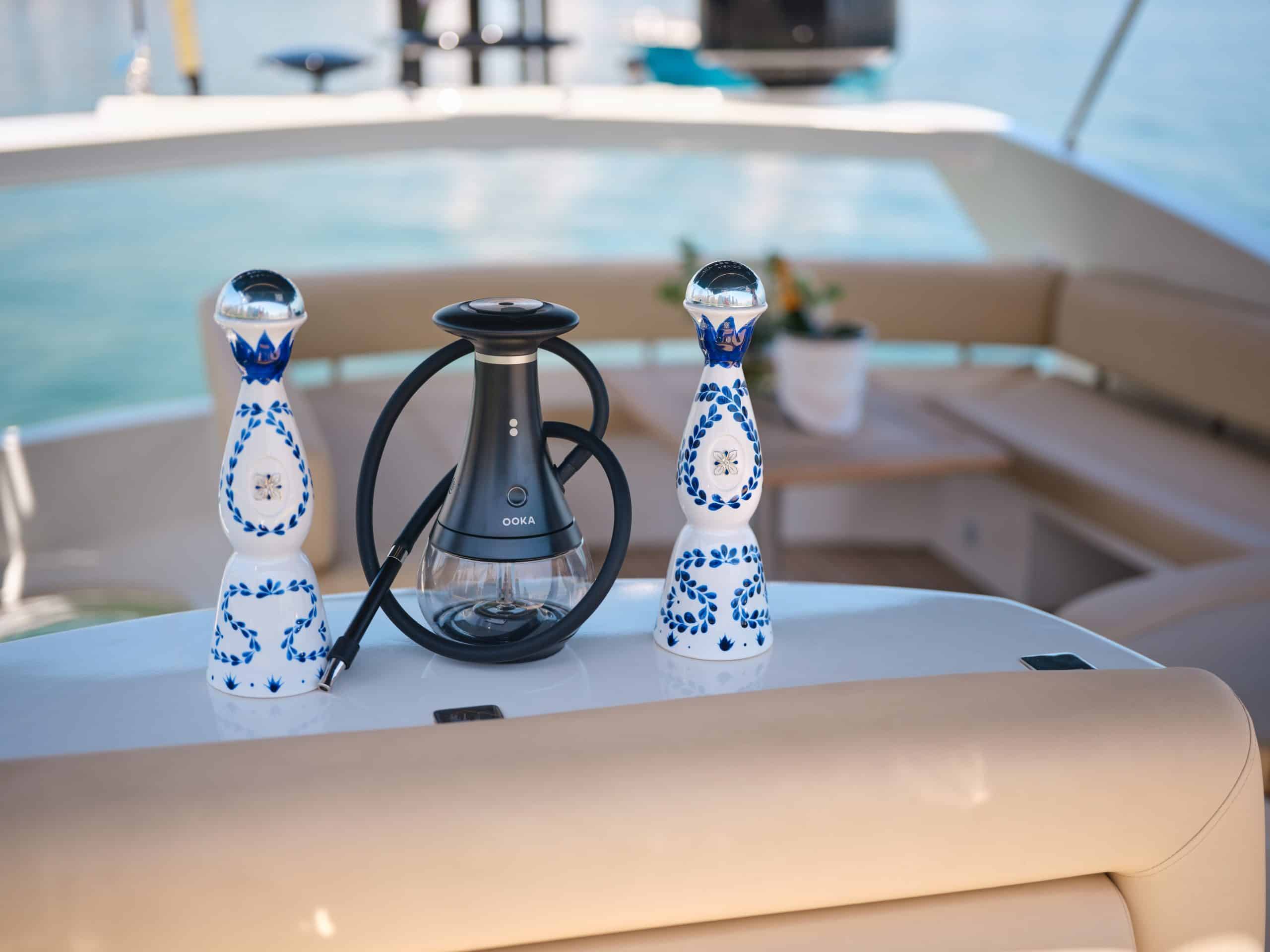 Modern OOKA hookah device with hose placed between two decorative ceramic bottles on a luxury yacht seating area.
