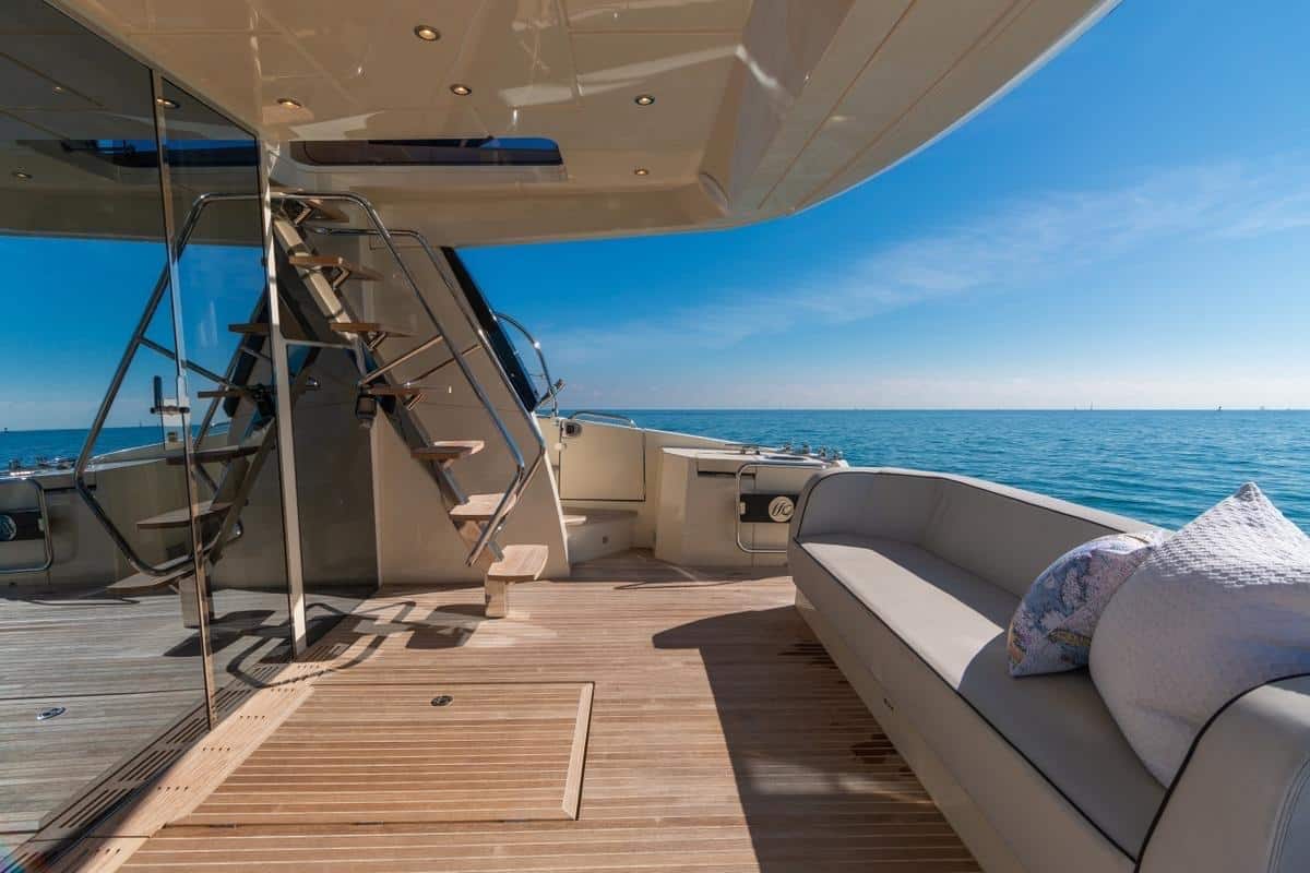 Luxury motor yacht aft deck with teak flooring, built-in lounge seating, staircase to flybridge, and open sea views