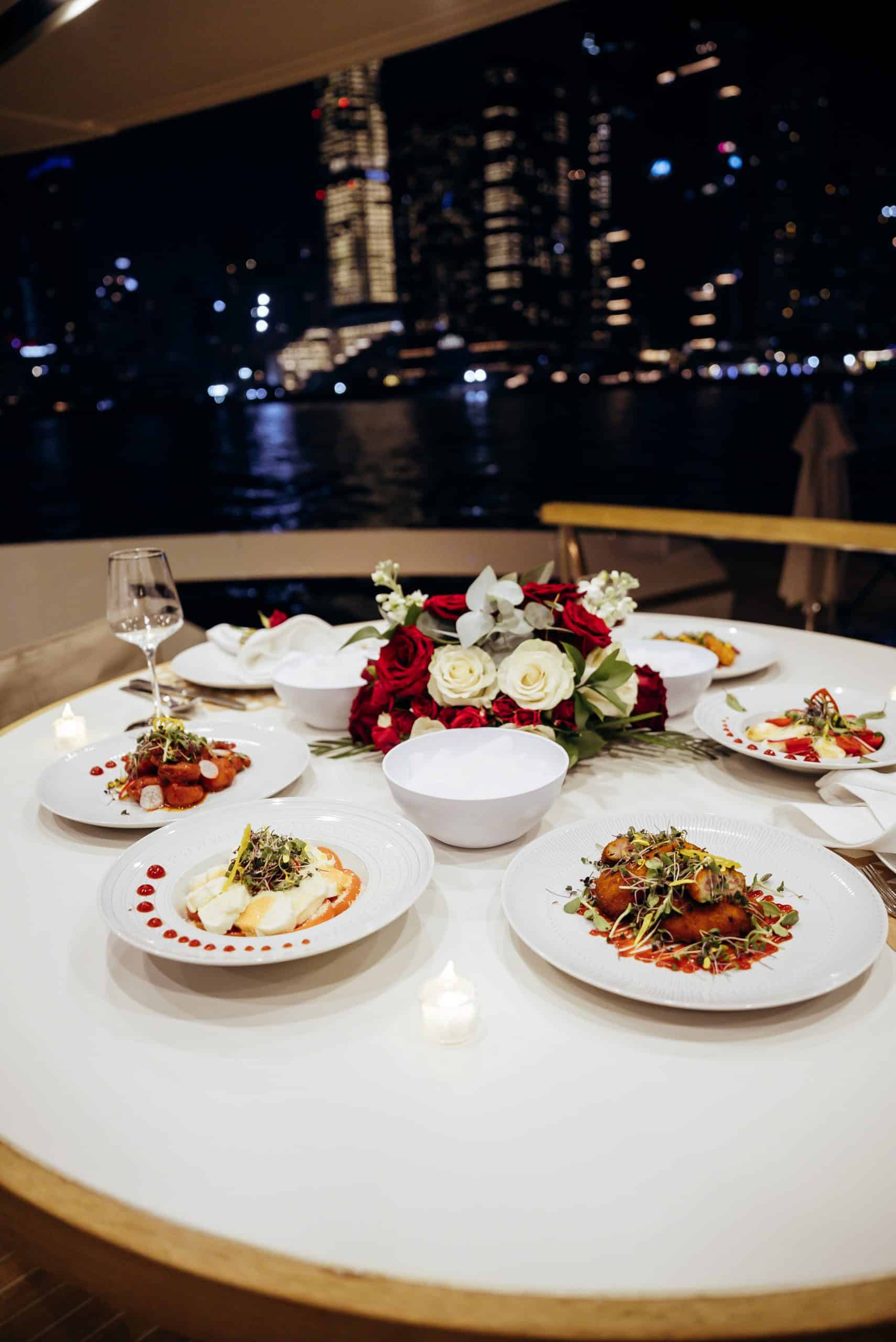 luxury yacht dinner setup at night with gourmet dishes and city skyline