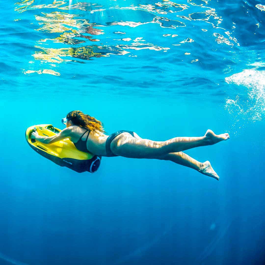 Person swimming underwater with a yellow Seabob scooter