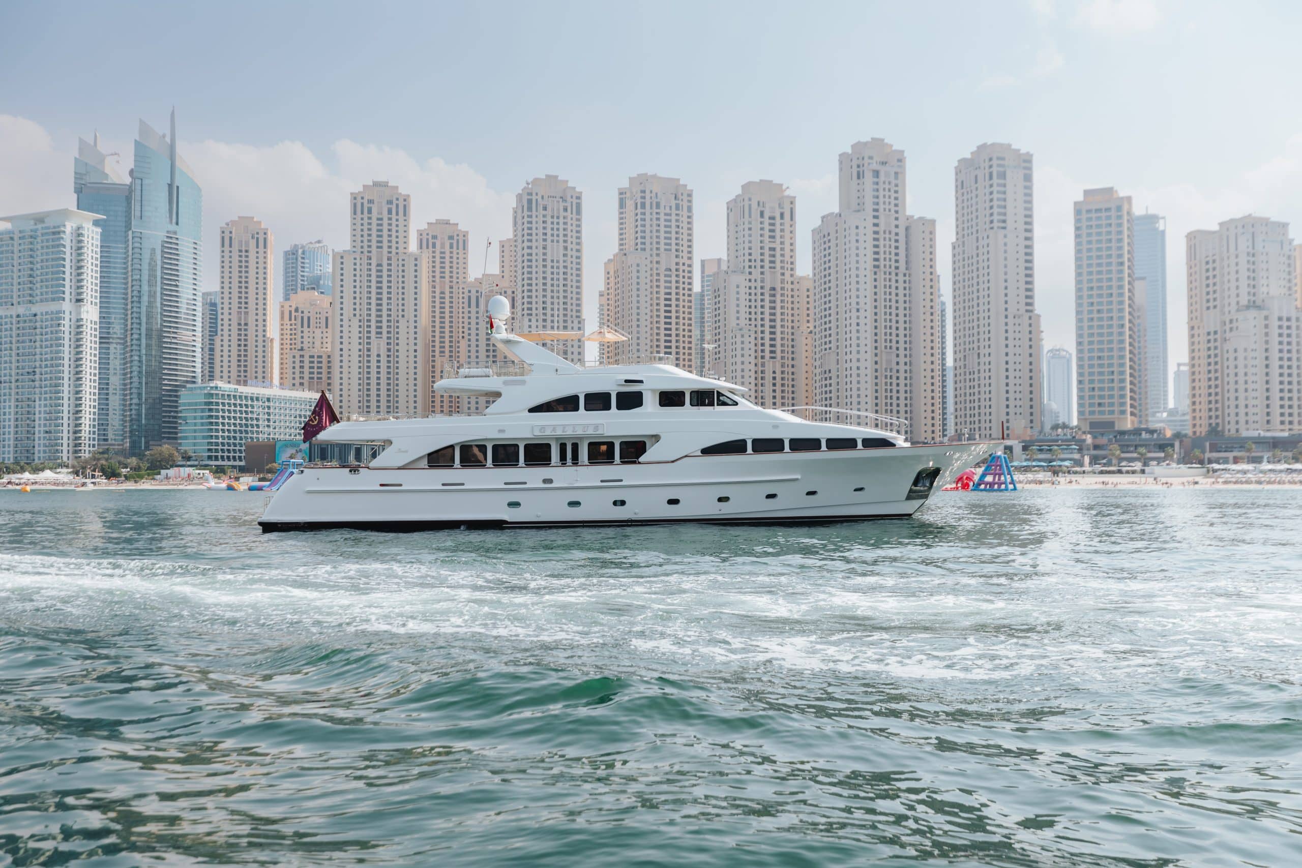 Luxury yacht cruising along the coastline of Dubai Marina, Dubai with high-rise skyline in the background.