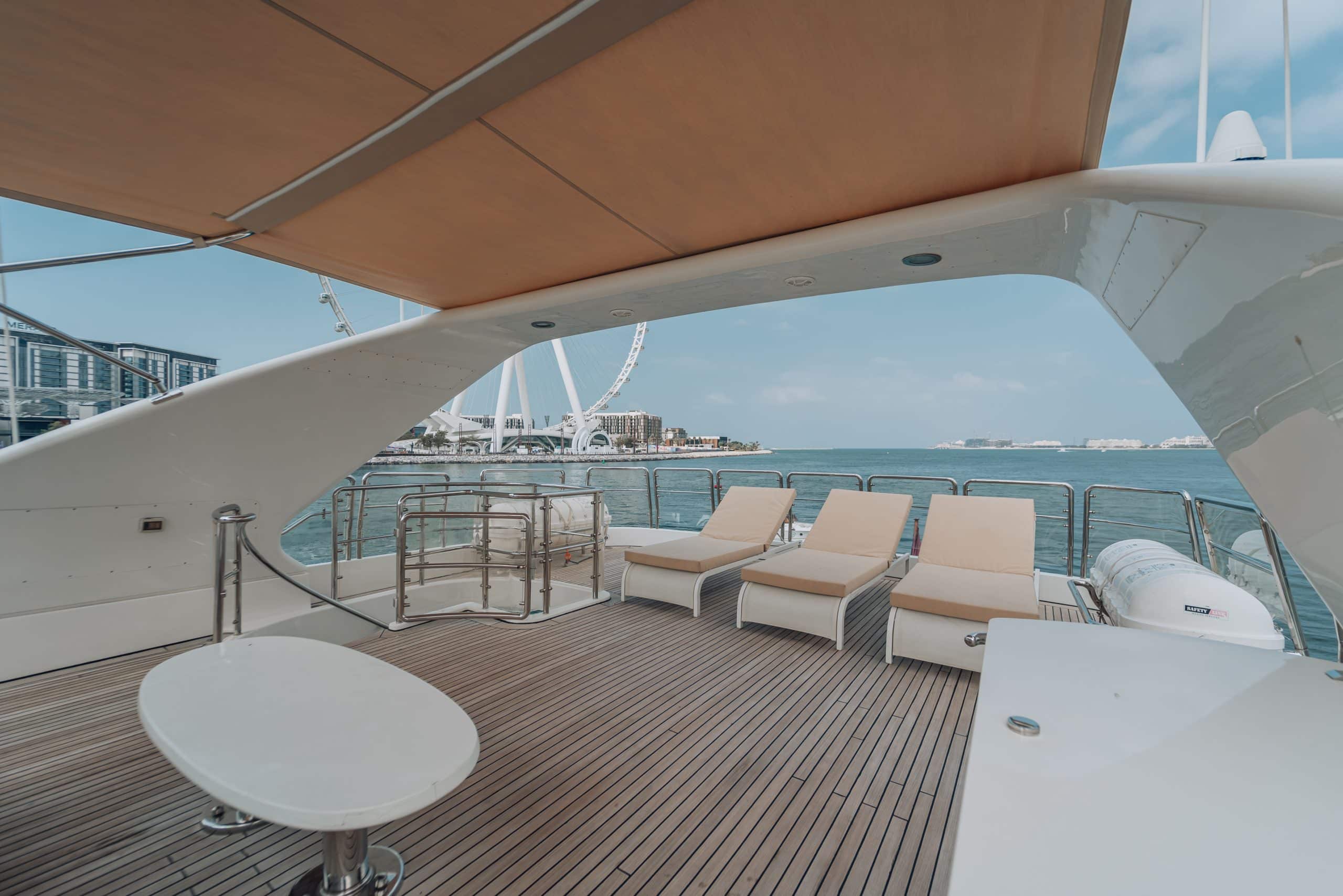 Luxury yacht deck with beige sun loungers under a canopy, overlooking turquoise water and Ain Dubai in the distance.