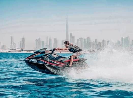 Rider carving a turn on a black and red jet ski with the Dubai skyline and Burj Khalifa behind