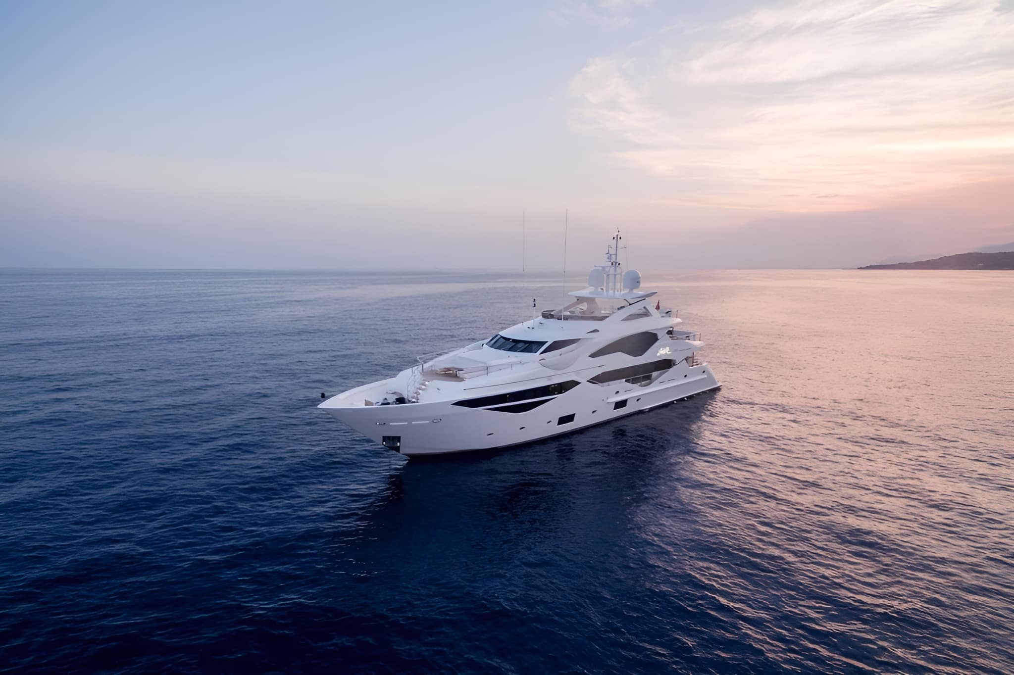 White superyacht cruising alone across calm open water under a soft pink dusk sky