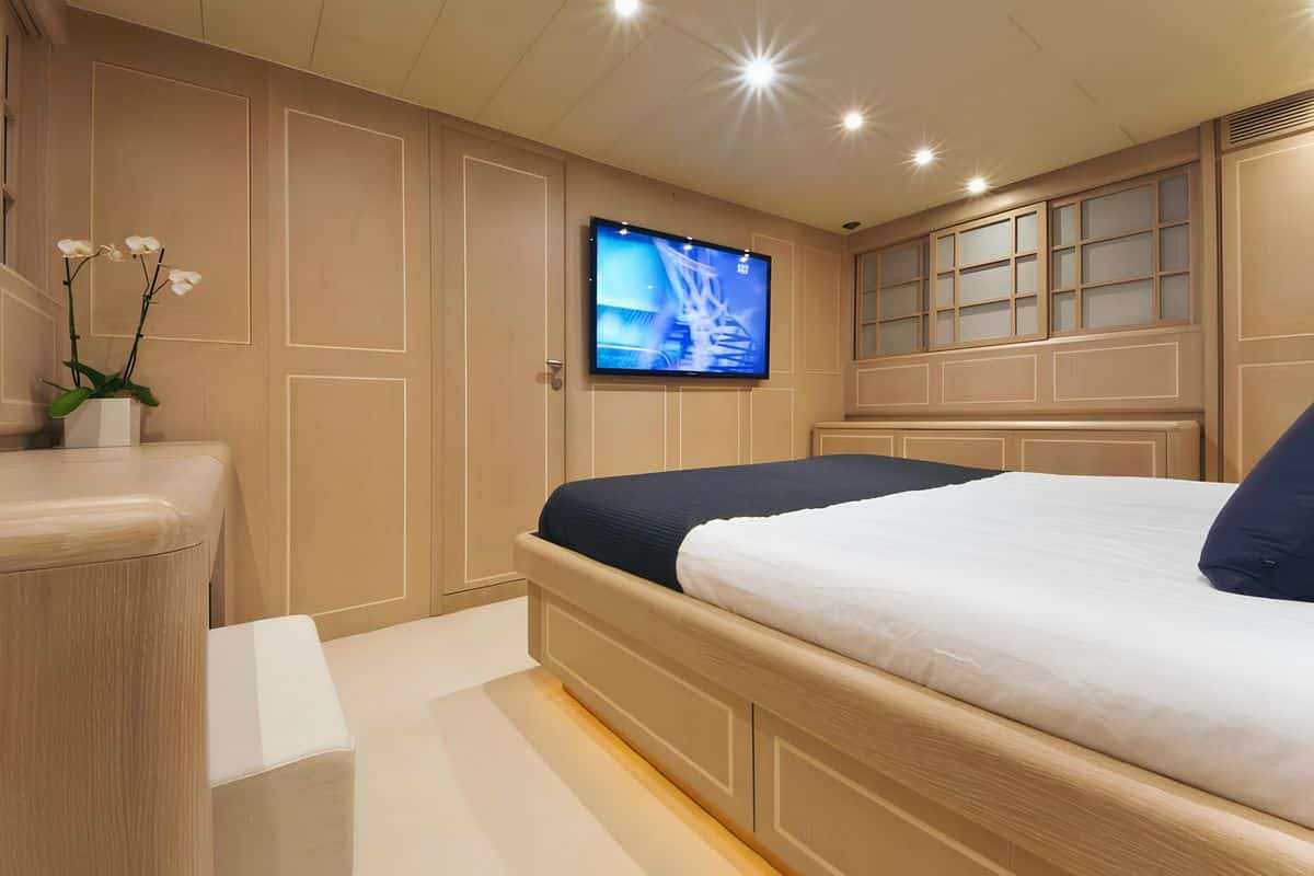 Luxury master cabin on Baglietto 110 yacht featuring wooden finishes, queen bed, and wall-mounted TV