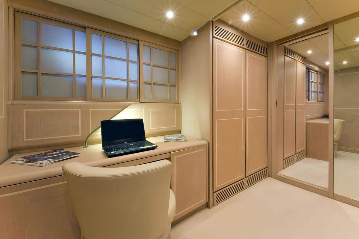 Baglietto 110 yacht interior vanity and workspace with wooden cabinetry, cushioned seating, and soft lighting