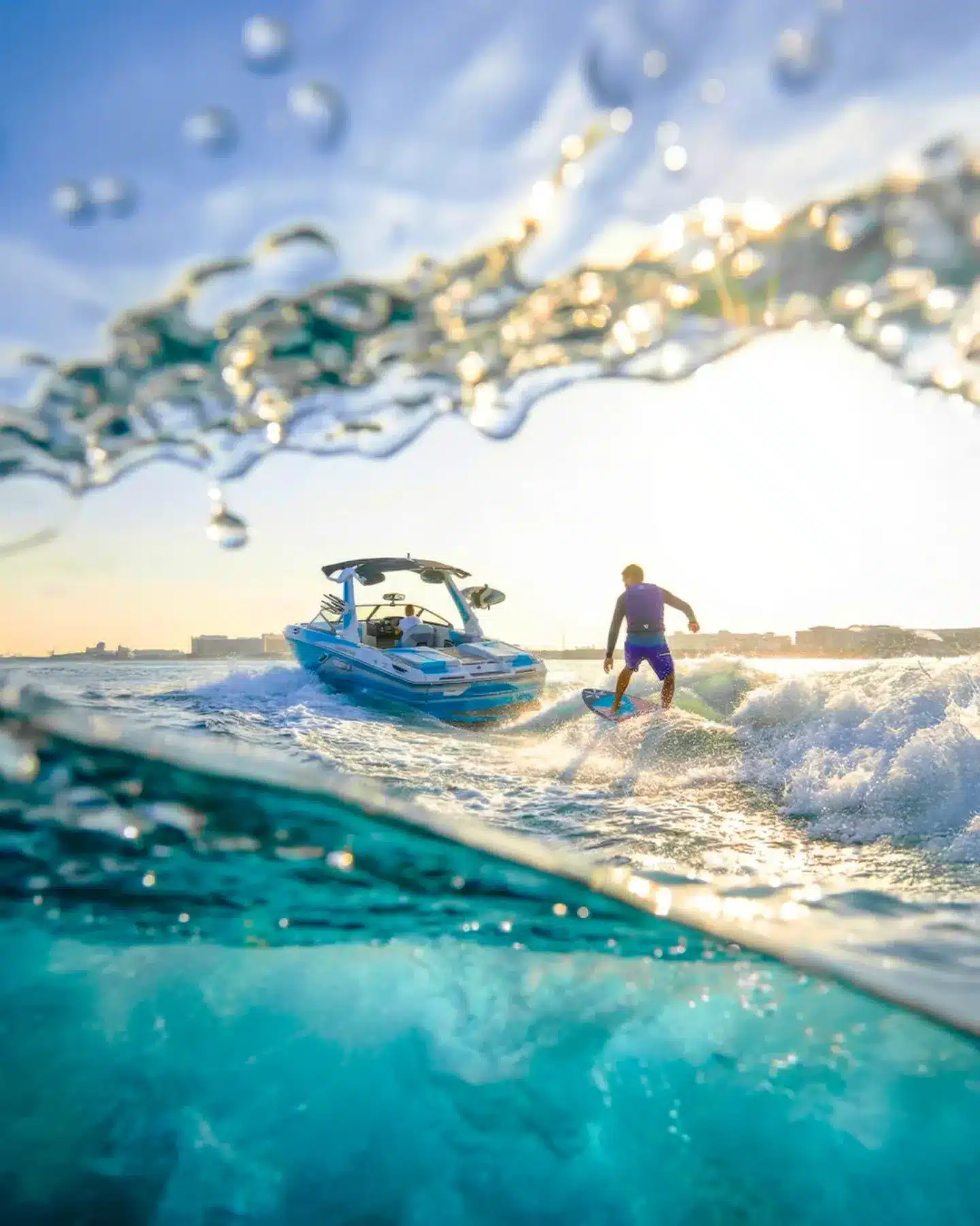 Split-level shot of a rider carving the wake behind a blue wake boat at golden hour