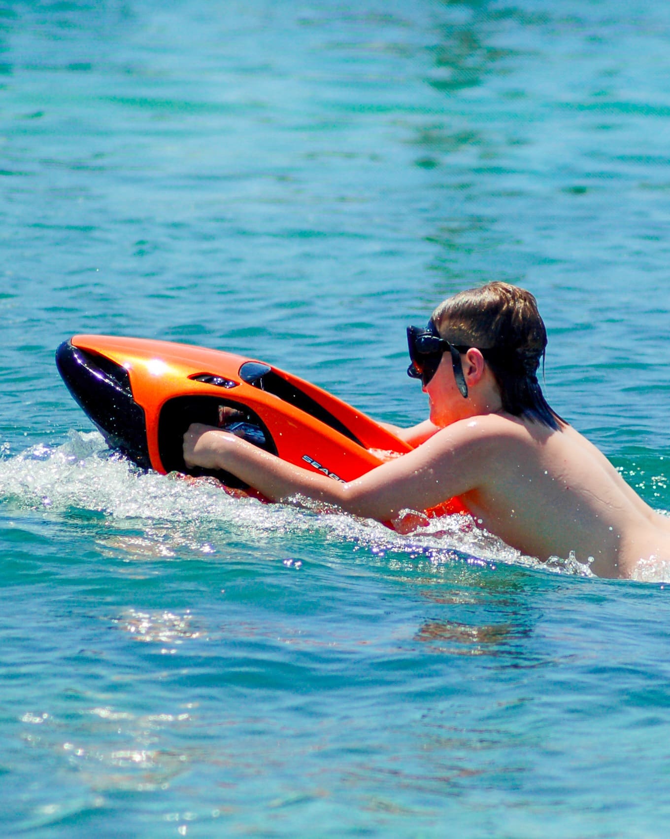 Man riding an orange Seabob water scooter on calm blue sea