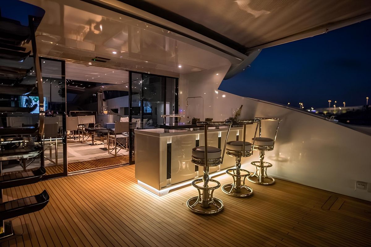 Baglietto 110 yacht outdoor deck bar with wooden flooring, modern stools, and ambient evening lighting at sea