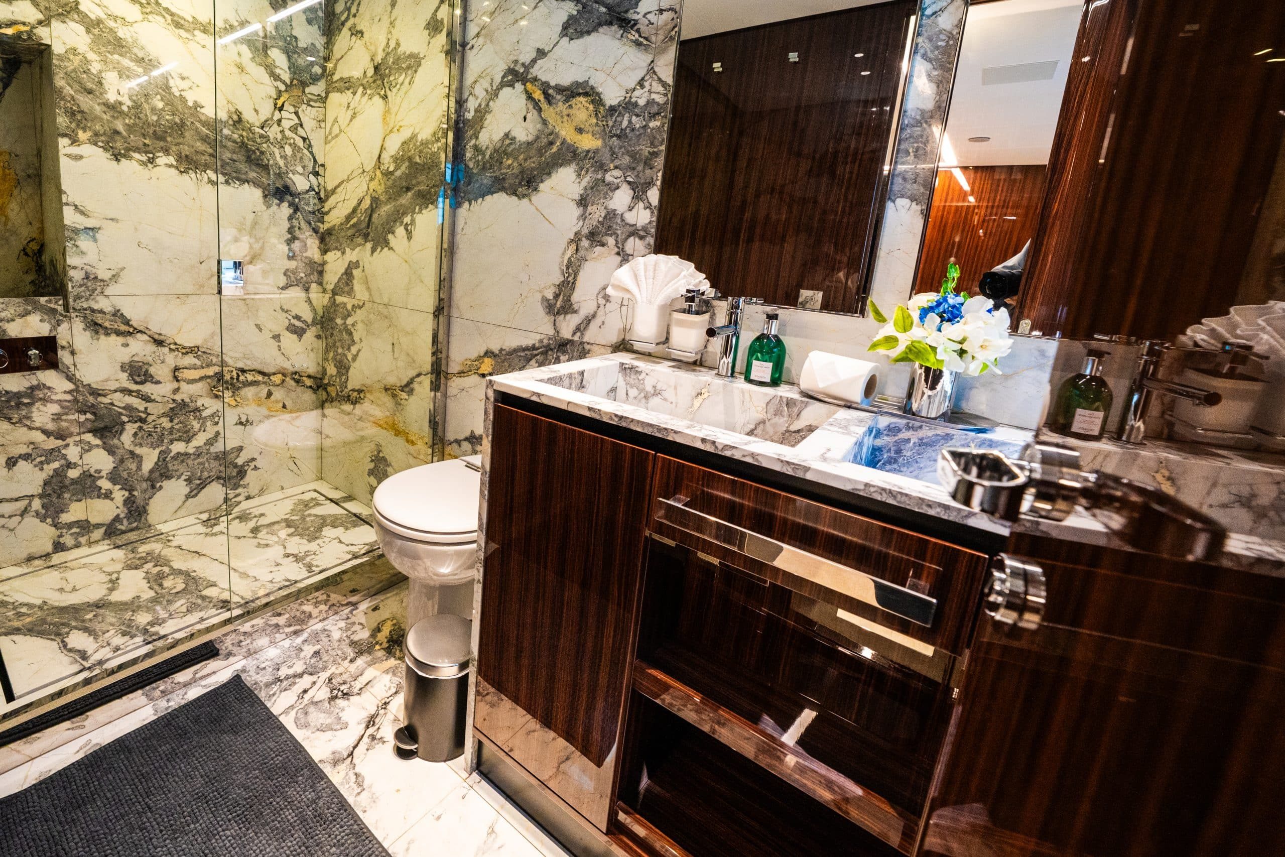 Luxury yacht bathroom with marble walls, glass shower, and glossy wood vanity