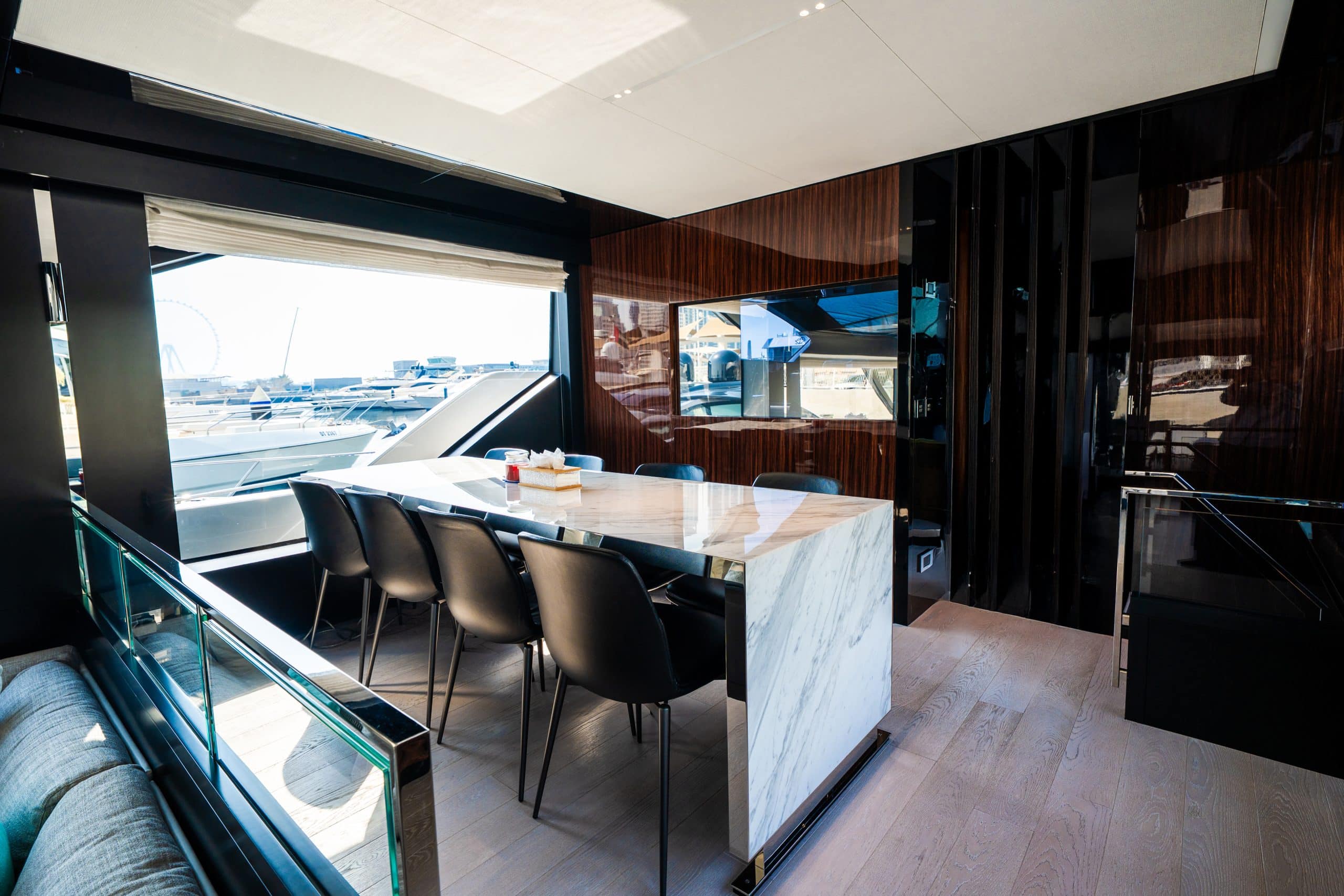 Riva 82 F1 yacht interior dining area with marble table, black leather chairs, and panoramic marina view