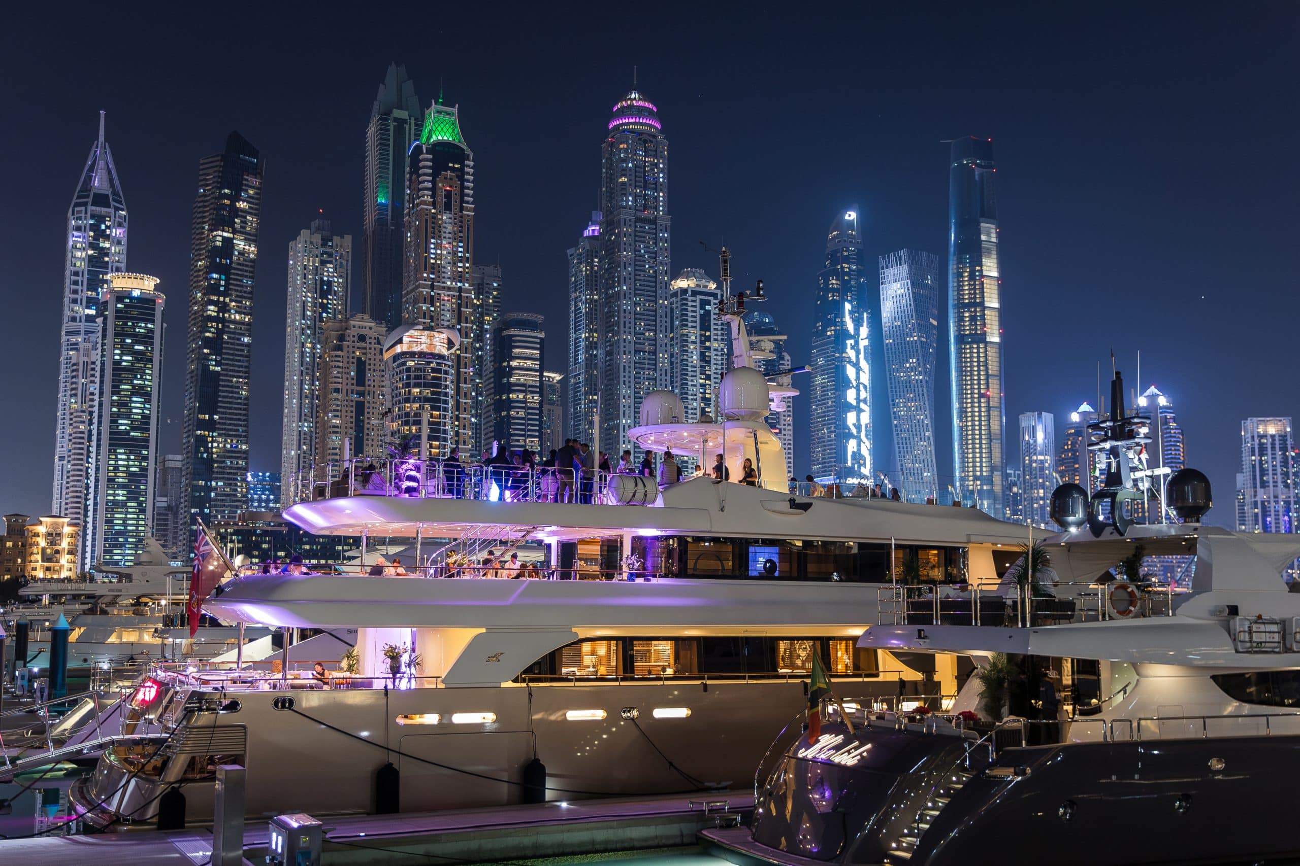 MILA 141 luxury yacht illuminated at night with Abu Dhabi skyline backdrop
