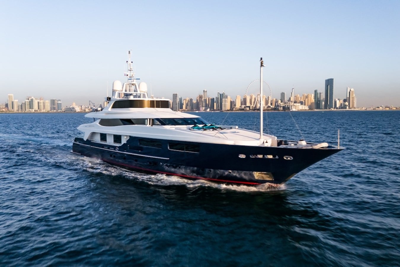 54m Baglietto superyacht under way on calm blue water with a high-rise city skyline on the horizon