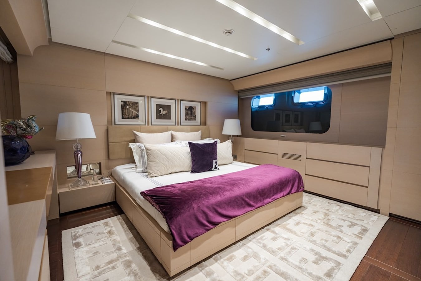 Yacht guest cabin with a double bed, purple throw, framed prints above the headboard and light oak joinery