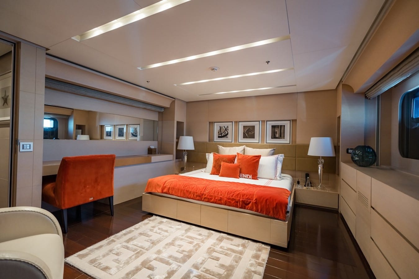 Yacht guest cabin with orange bedspread and matching armchair at a built-in vanity desk
