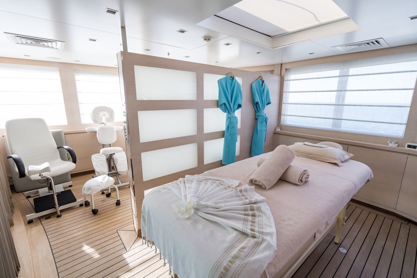 Onboard spa room with a massage table, rolled towels, turquoise robes and a pedicure chair