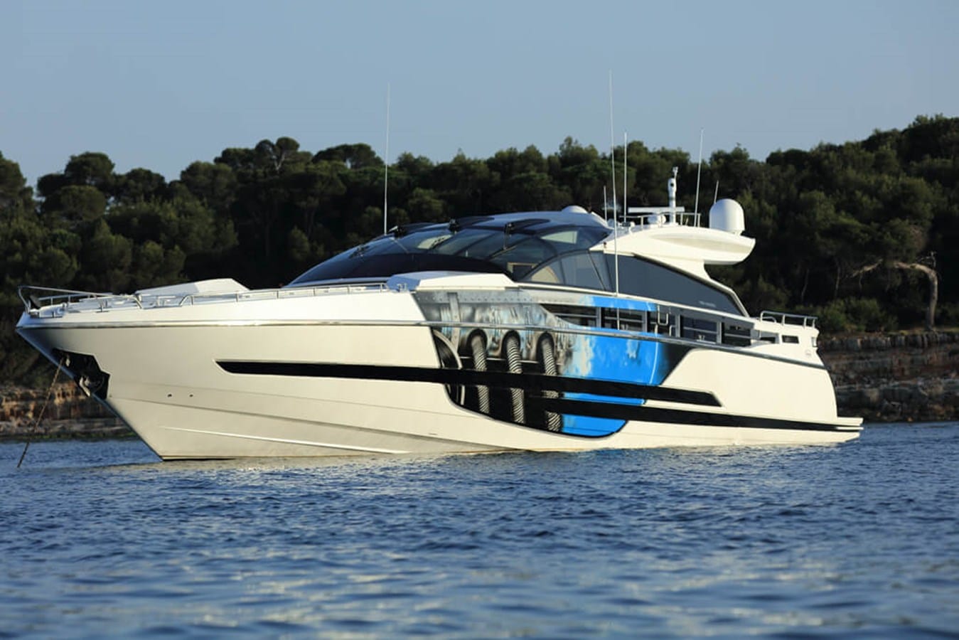 Baia 100 profile at anchor off a wooded Mediterranean coastline